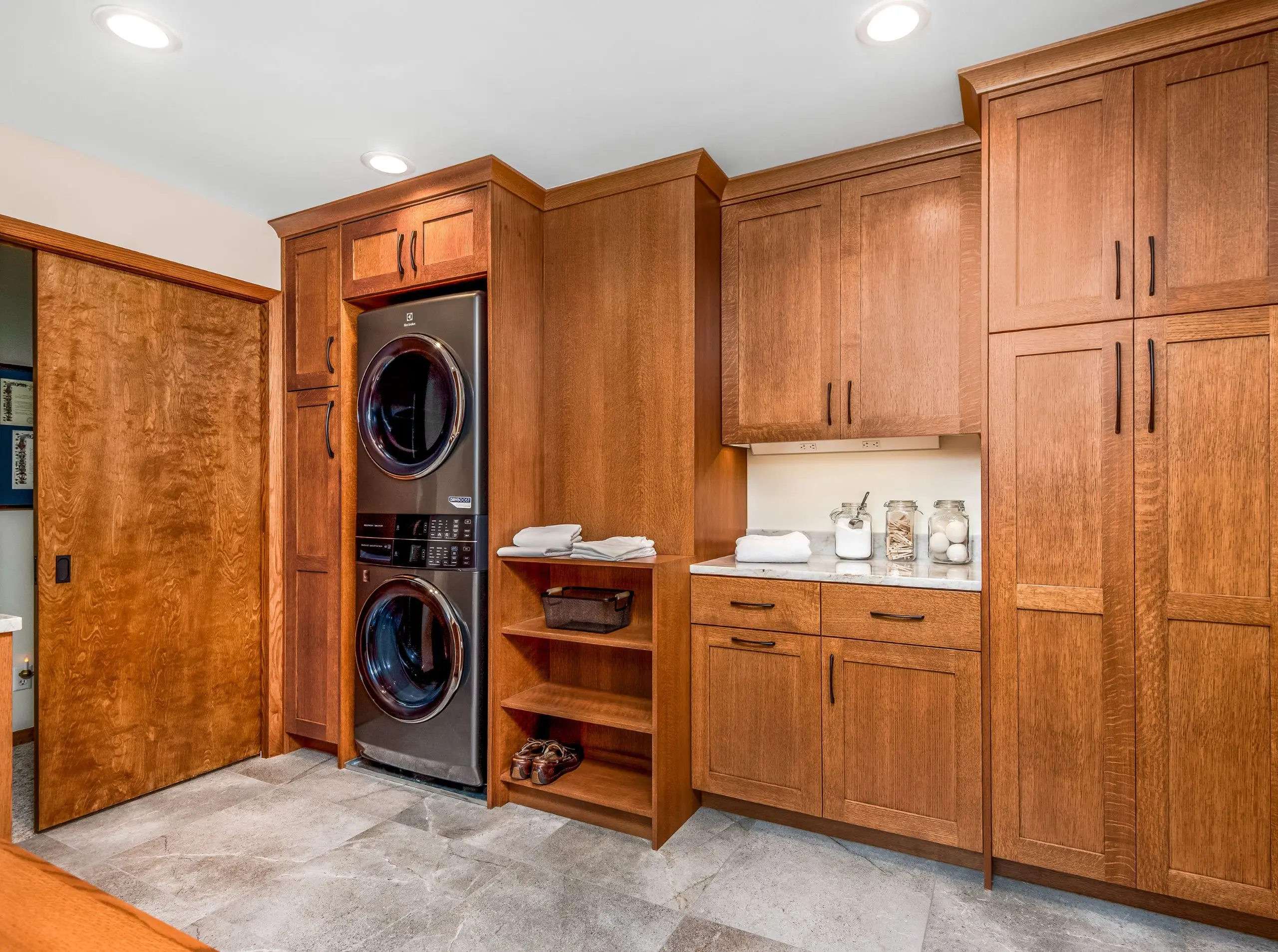 wood cabinetry in laundry room with stacked laundry, open and closed shelving, pocket door