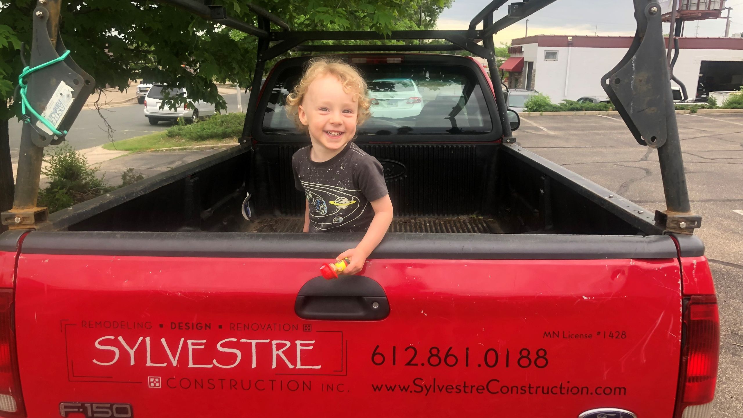 what's the story - young boy curly hair and smiling in back of red pickup truck