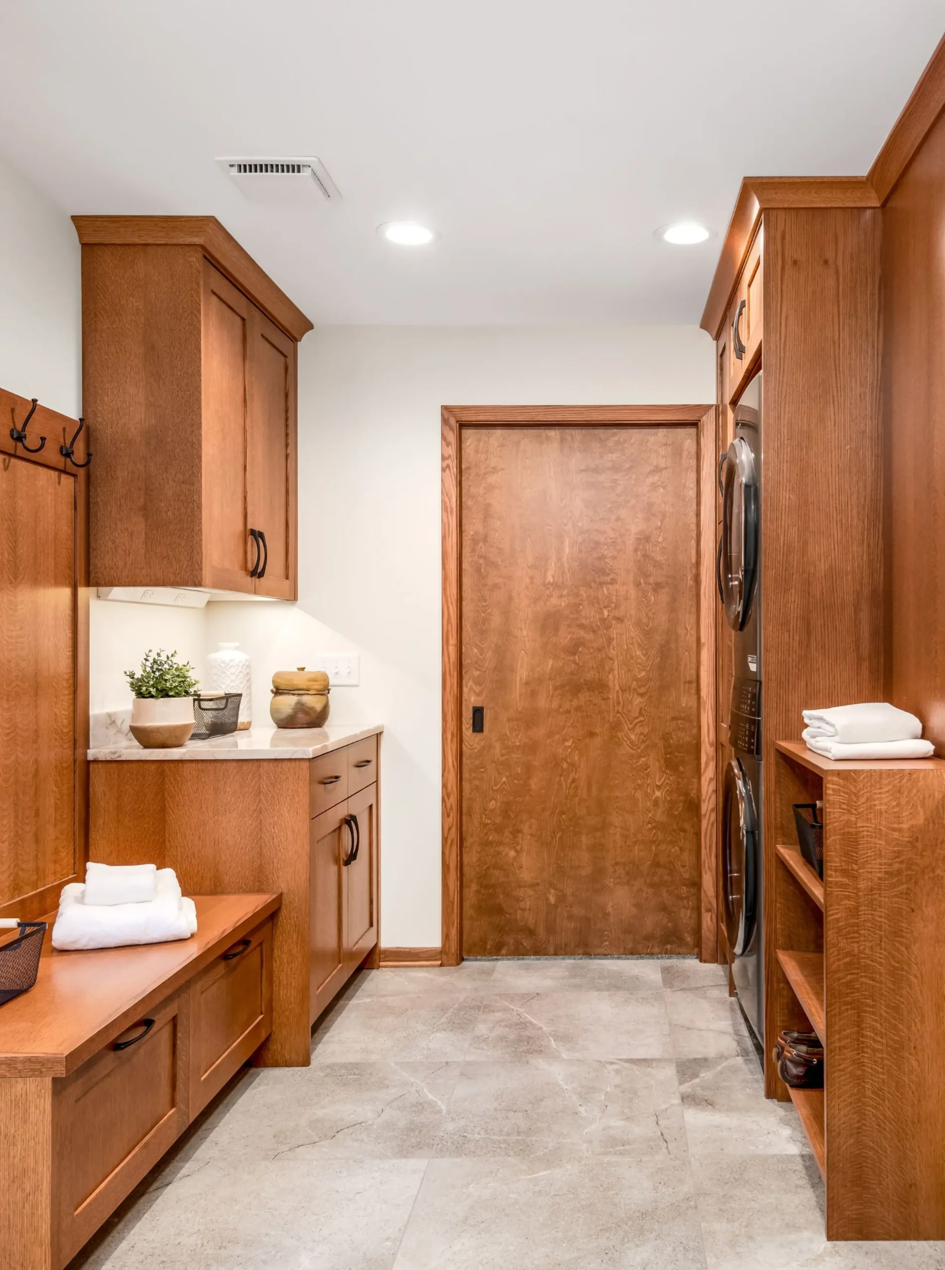 laundry room with bench and cabinets, wide closed pocket door, stacked laundry 